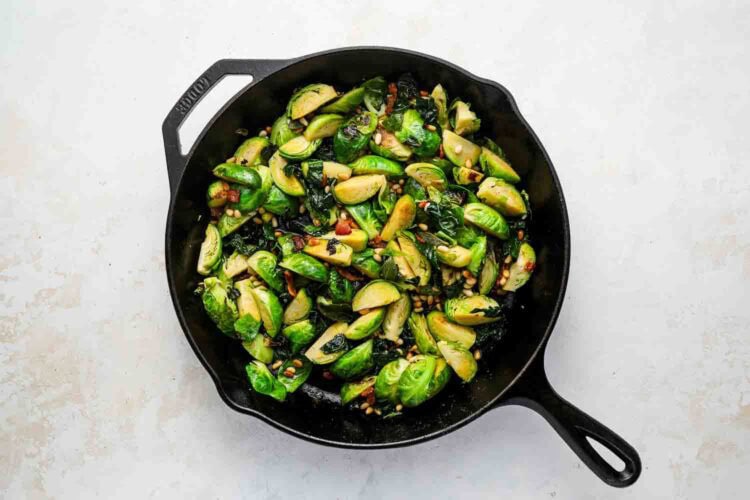 Sliced Brussels sprouts sautéed with herbs and spices in a black cast iron skillet, set on a light-colored surface.