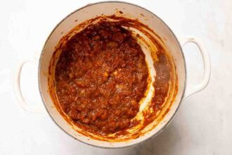 A white pot containing thick, chunky tomato sauce with visible diced onions and spices, partially coating the sides of the pot, perfect as a base for Marry Me Turkey Soup.