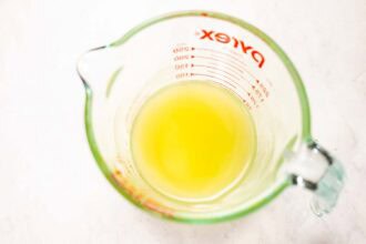 A glass measuring cup containing a yellow liquid, possibly for a Pourhouse Caesar, is placed on a white surface.