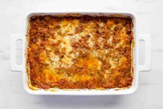 A baked Zucchini Lasagna in a white rectangular dish, showing a browned, cheesy top layer with visible meat sauce.