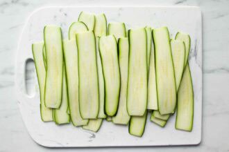 Sliced zucchini arranged in a single layer on a white cutting board.