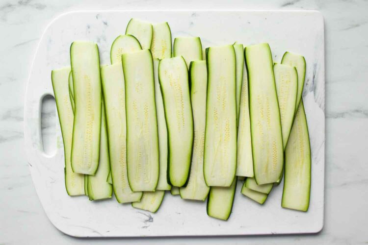 Sliced zucchini arranged in a single layer on a white cutting board.