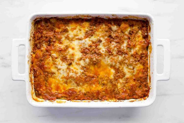 A baked Zucchini Lasagna in a white rectangular dish, showing a browned, cheesy top layer with visible meat sauce.
