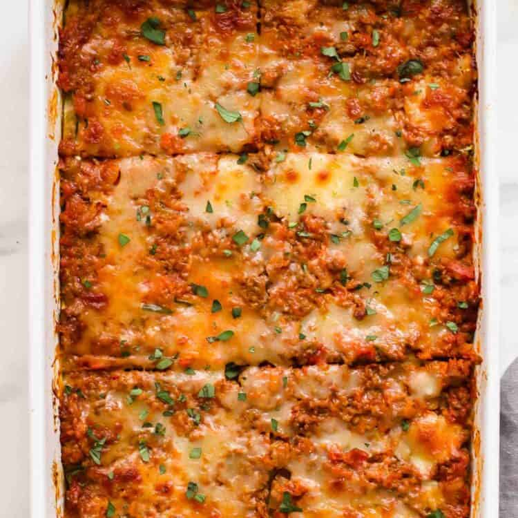 A baked Zucchini Lasagna in a white rectangular dish, topped with melted cheese and herbs, cut into twelve square pieces.