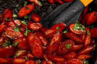 Sticky ginger soy glazed carrots garnished with chopped parsley in a pan, with a black spatula beside them.