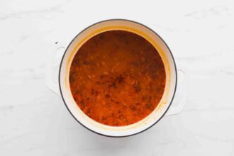 A white pot filled with rich Marry Me Chicken Soup, sprinkled with herbs, sits on a white marble surface.