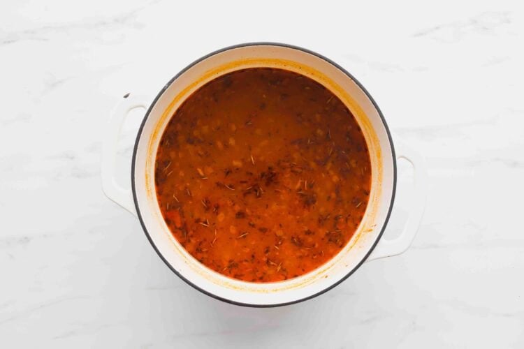 A white pot filled with rich Marry Me Chicken Soup, sprinkled with herbs, sits on a white marble surface.