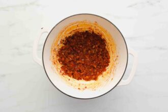 A white pot containing sautéed diced vegetables, including onions and carrots, cooked with tomato paste on a white marble surface—the perfect base for a comforting Marry Me Chicken Soup.