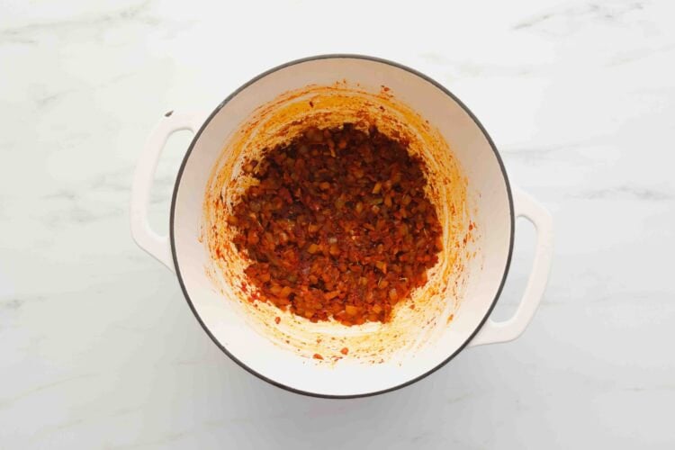 A white pot containing sautéed diced vegetables, including onions and carrots, cooked with tomato paste on a white marble surface—the perfect base for a comforting Marry Me Chicken Soup.