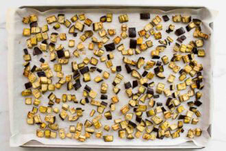 A baking sheet lined with parchment paper holds evenly spaced, roasted cubes of eggplant, perfect for making classic dishes like Pasta alla Norma or your favorite eggplant pasta.