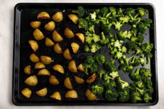 A sheet pan with seasoned potato wedges on the left and broccoli florets on the right, both arranged in separate sections before roasting.