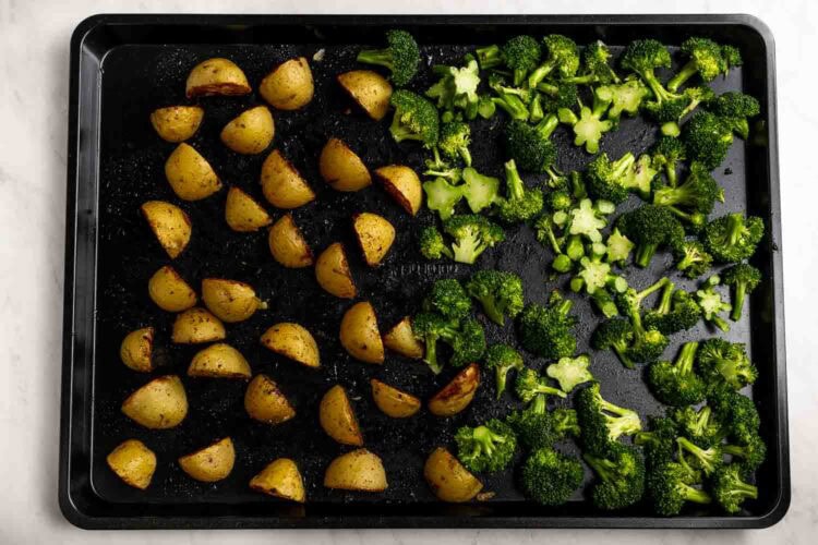 A sheet pan with seasoned potato wedges on the left and broccoli florets on the right, both arranged in separate sections before roasting.