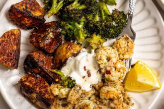 A plate with roasted potatoes, shrimp and broccoli in herbs, a dollop of sour cream, and a lemon wedge makes for a flavorful sheet pan dinner.