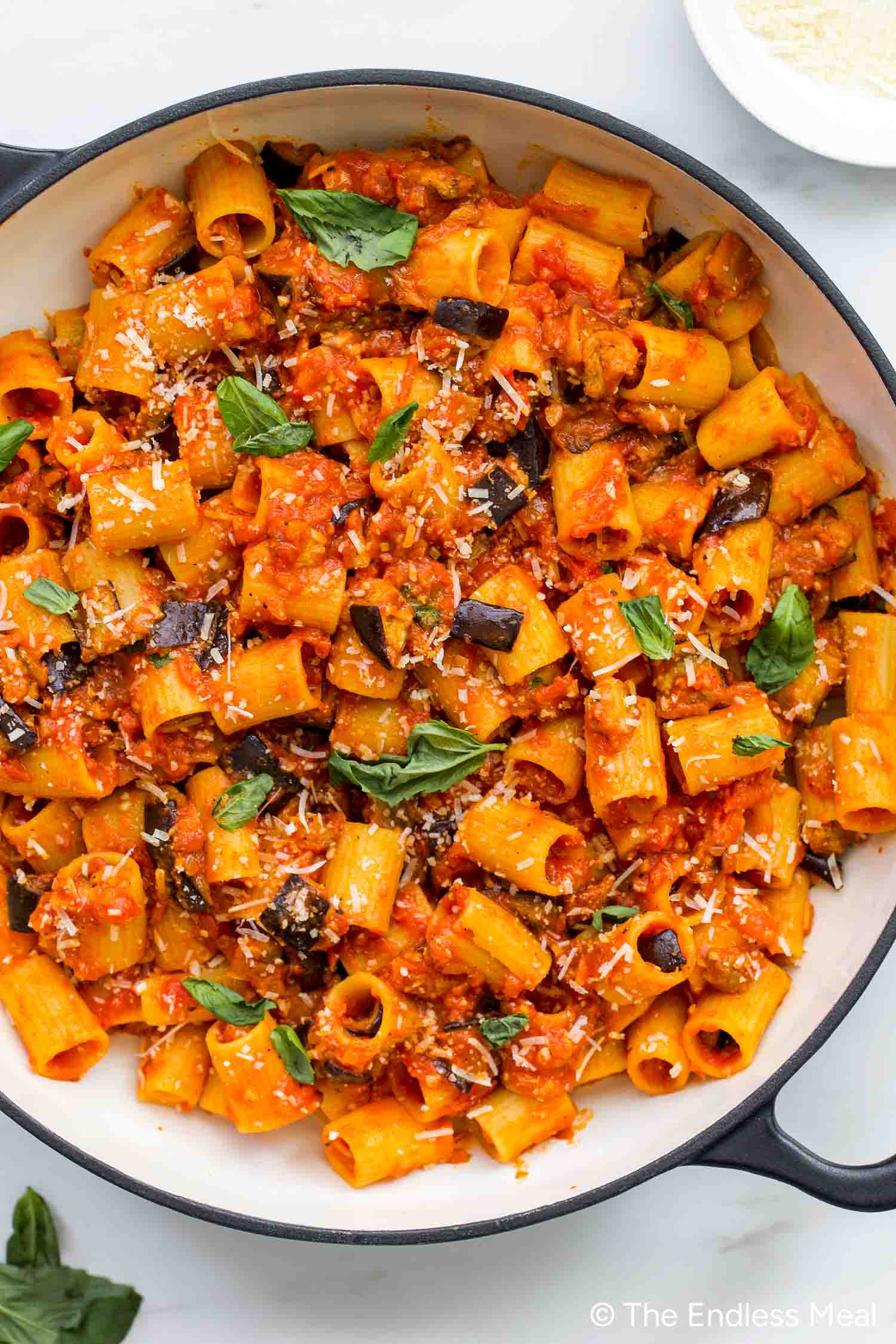 A pan filled with delicious Pasta alla Norma—rigatoni in rich tomato sauce, topped with grated cheese, chopped eggplant, and fresh basil leaves.
