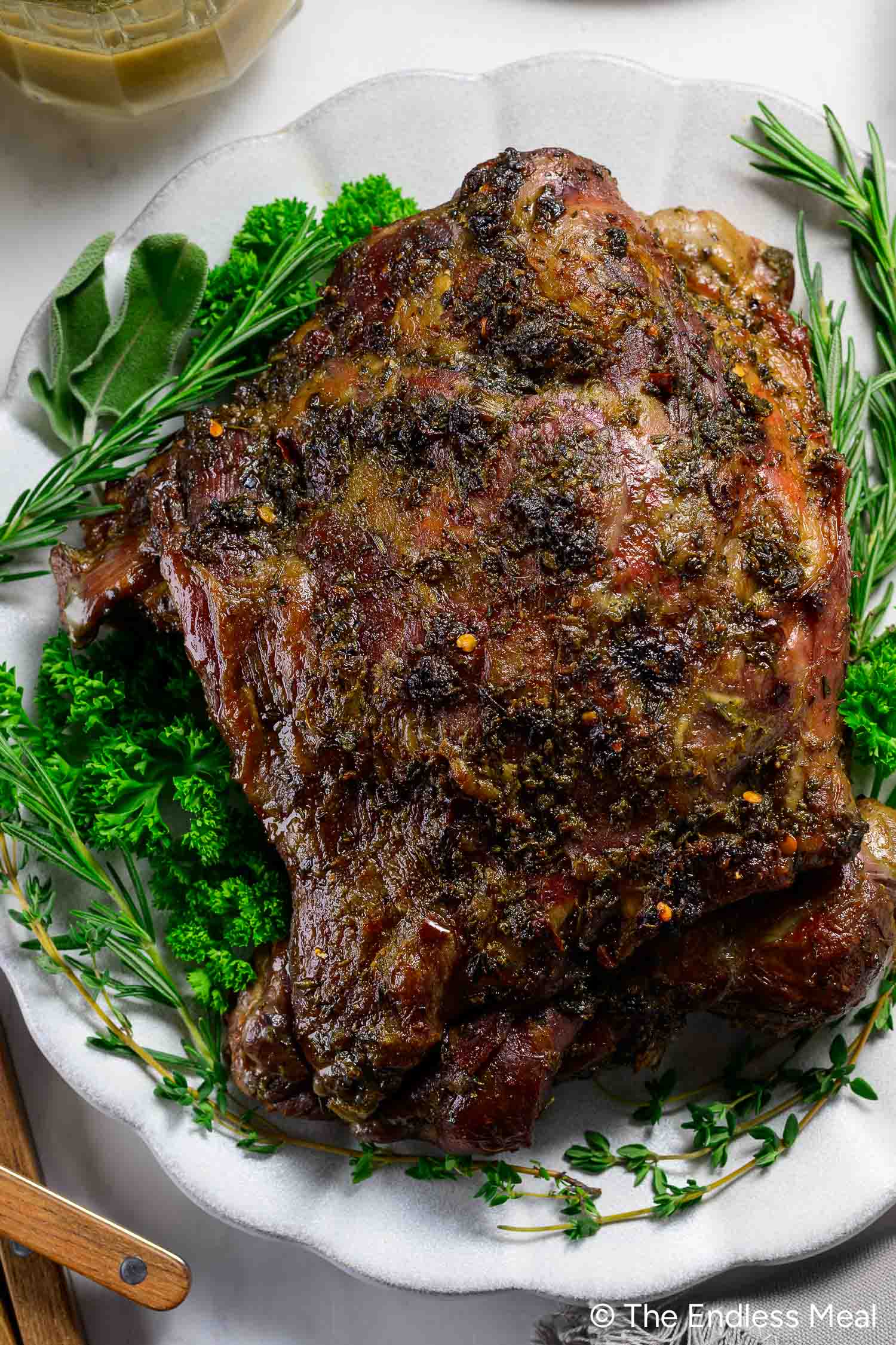 Oven Braised Leg of Lamb garnished with fresh parsley and rosemary, served on a white platter.