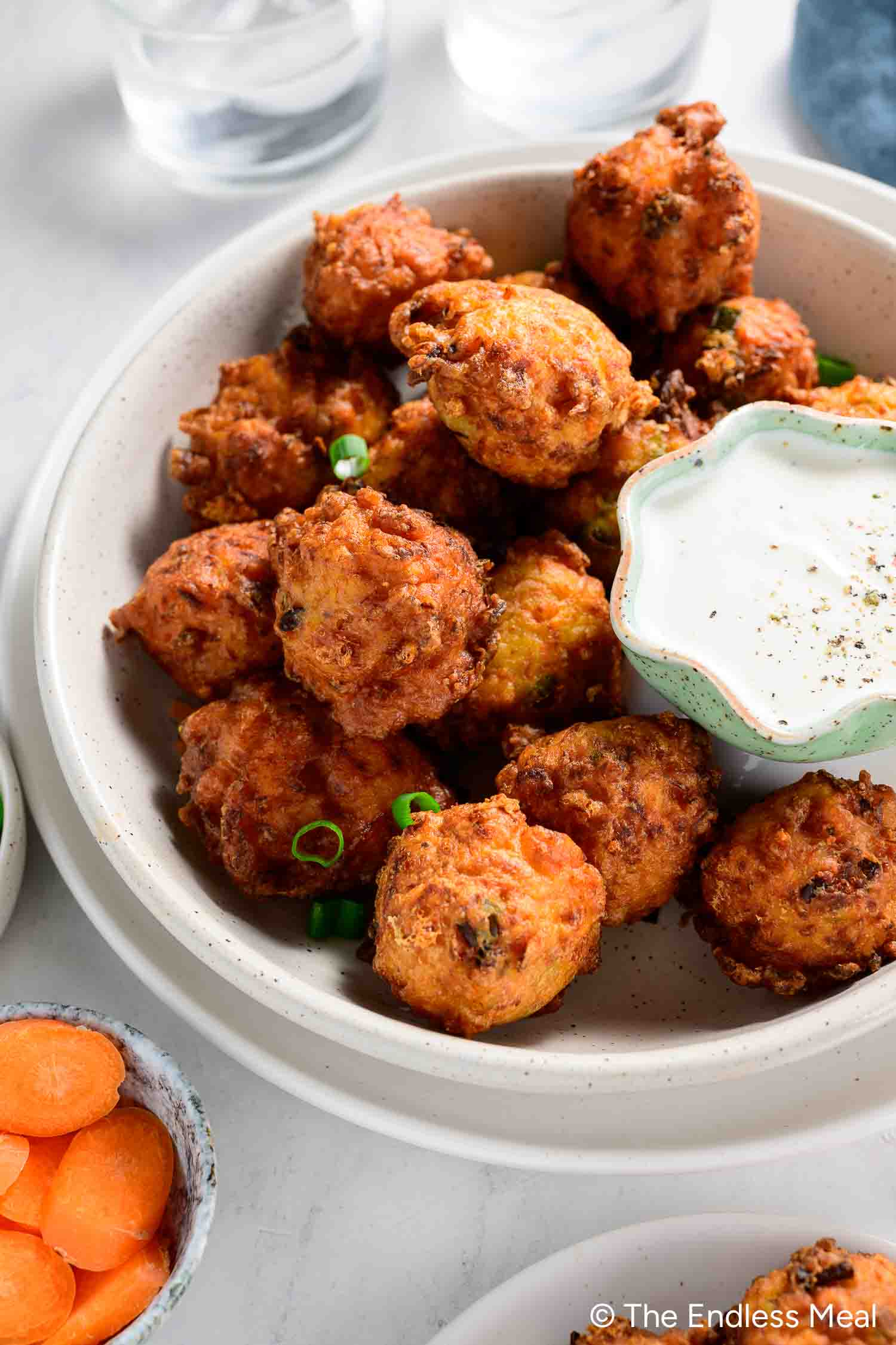 A bowl of golden-brown carrot fritters garnished with green onions, served with a side of white dipping sauce—a delicious addition to your favorite carrot recipes.