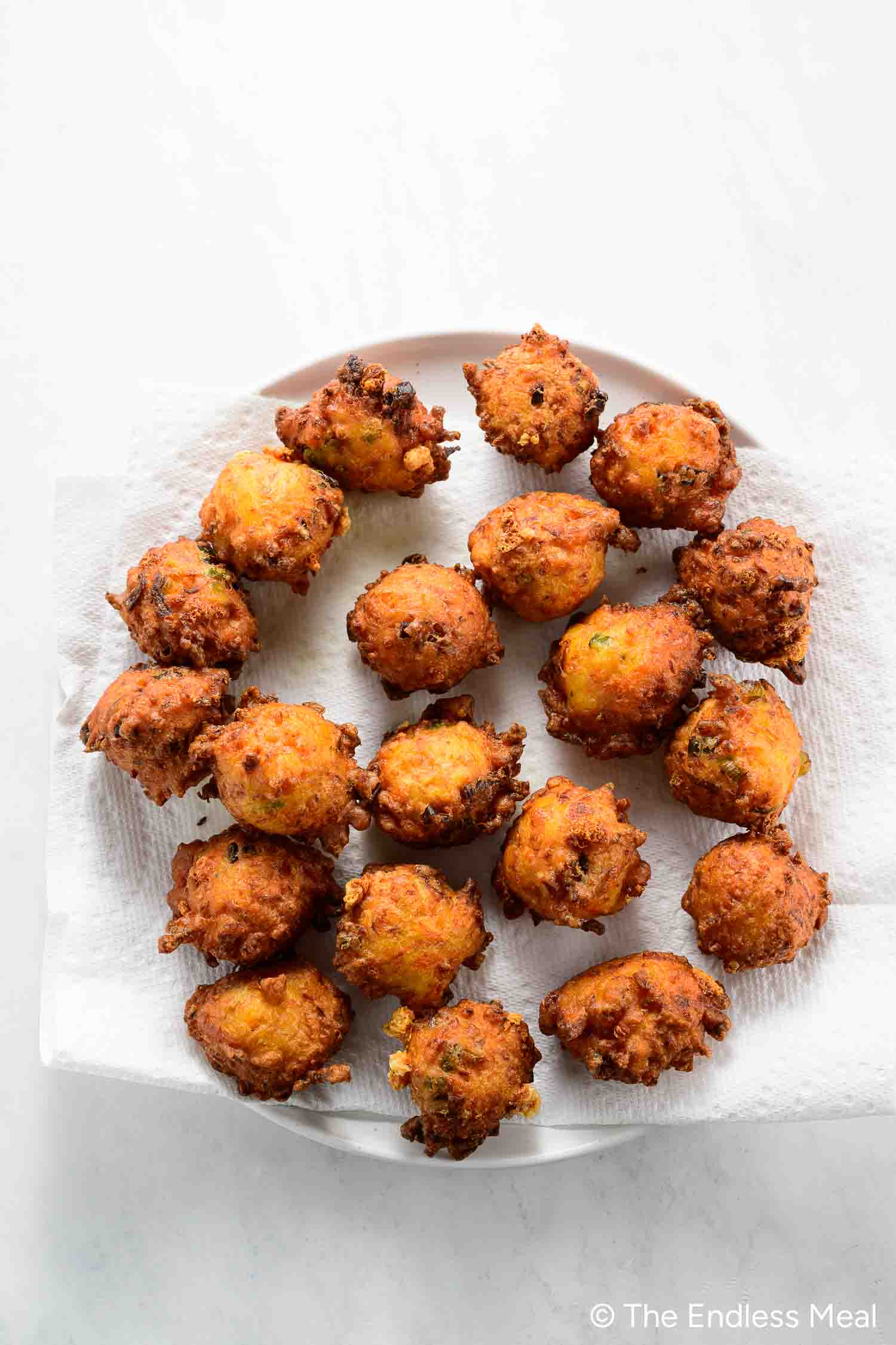 A plate lined with paper towels holds several golden-brown carrot fritters arranged in a circle on a white surface, making them a perfect choice for healthy snacks and delicious carrot recipes.