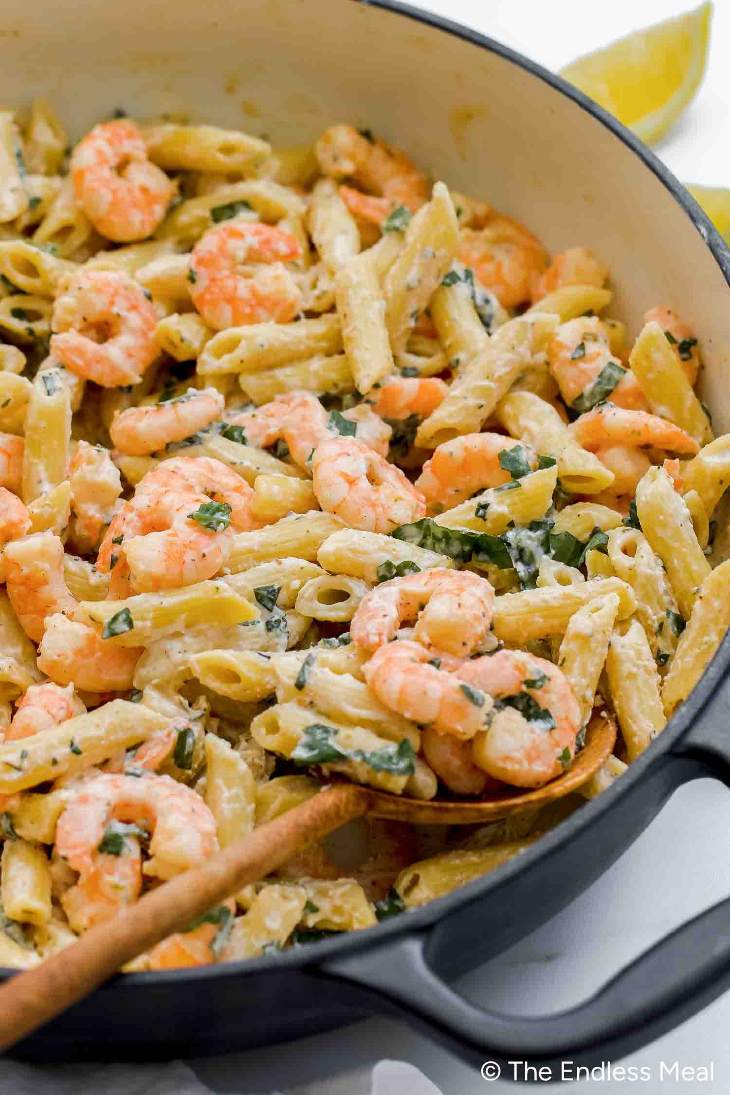 Penne pasta with shrimp and fresh herbs in a lemony, creamy ricotta pasta sauce, served in a white pot with a wooden spoon.