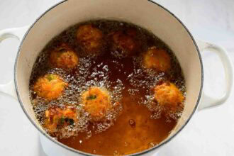 Seven golden-brown carrot fritters are deep frying in hot oil inside a white pot, perfect for trying new carrot recipes.