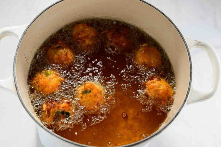 Seven golden-brown carrot fritters are deep frying in hot oil inside a white pot, perfect for trying new carrot recipes.