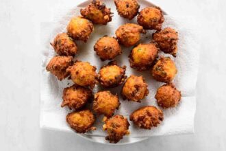 A plate lined with paper towels holds several golden-brown vegetable fritters arranged in a circular pattern.
