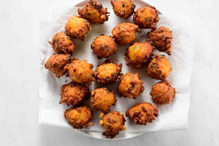 A plate lined with paper towels holds several golden-brown vegetable fritters arranged in a circular pattern.