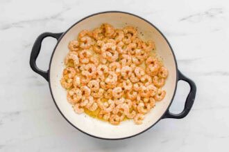 Cooked shrimp in a white, round skillet with black handles, seasoned and resting in oil on a white marble surface—perfect for pairing with Lemony Ricotta Pasta Sauce.