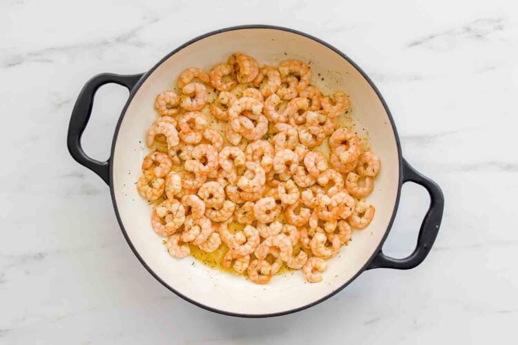 Cooked shrimp in a white, round skillet with black handles, seasoned and resting in oil on a white marble surface—perfect for pairing with Lemony Ricotta Pasta Sauce.