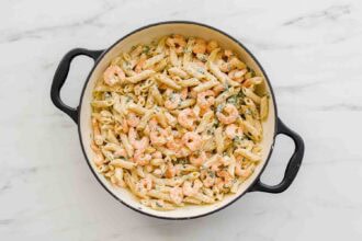 Large pot filled with cooked penne pasta and shrimp in a creamy, Lemony Ricotta Pasta Sauce with herbs, placed on a white marble surface.