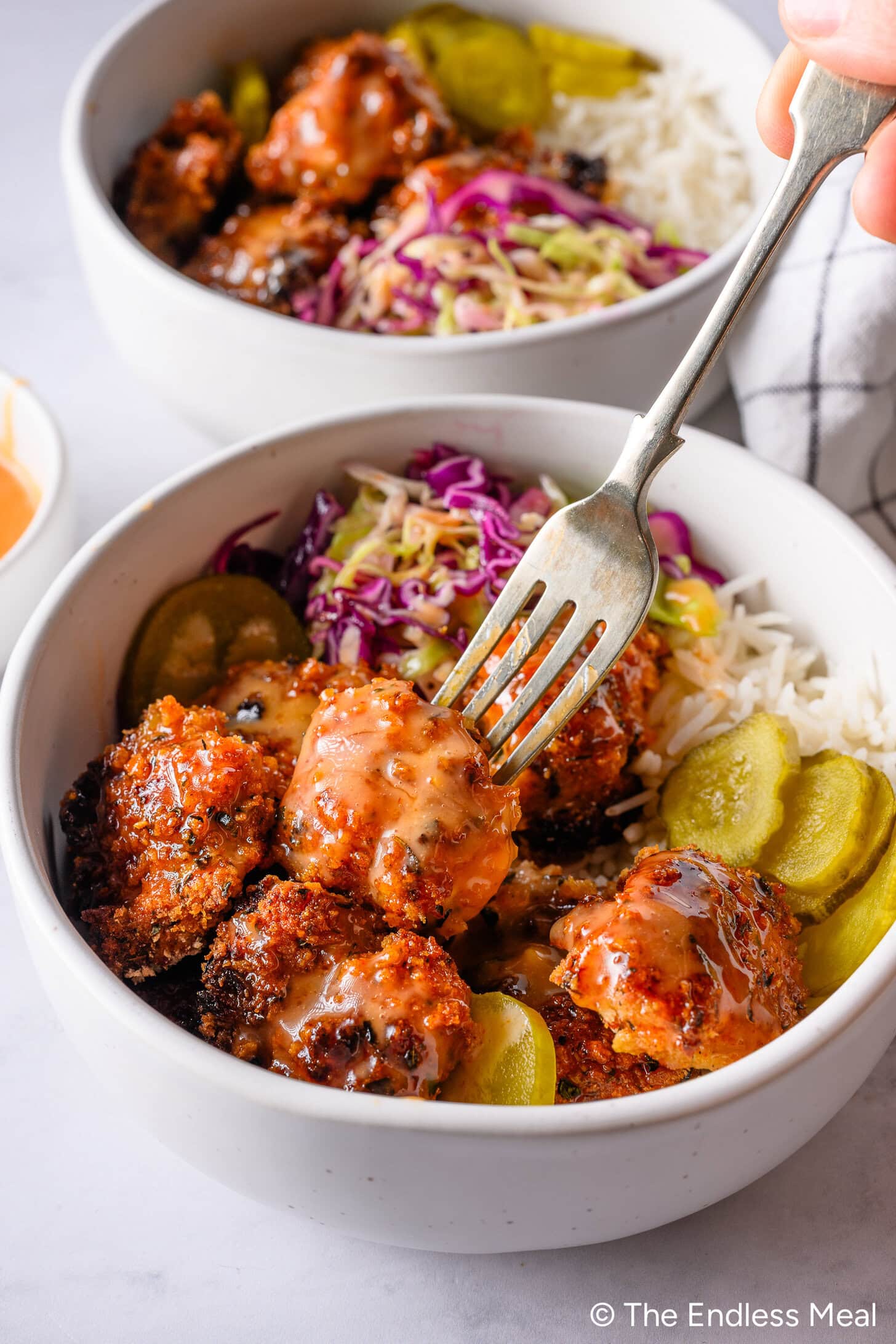 A bowl of crispy chicken pieces with sauce, rice, pickles, and shredded purple cabbage—perfect for your Endless Meal Cooking Club dinner. A fork is picking up a piece of chicken, ready to enjoy this May 2026 delight.