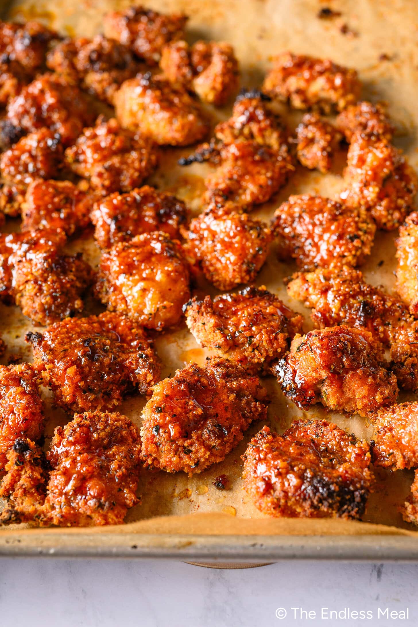 A baking sheet from the Endless Meal Cooking Club is covered with crispy, breaded chicken bites coated in a reddish sauce, arranged in neat rows on parchment paper.