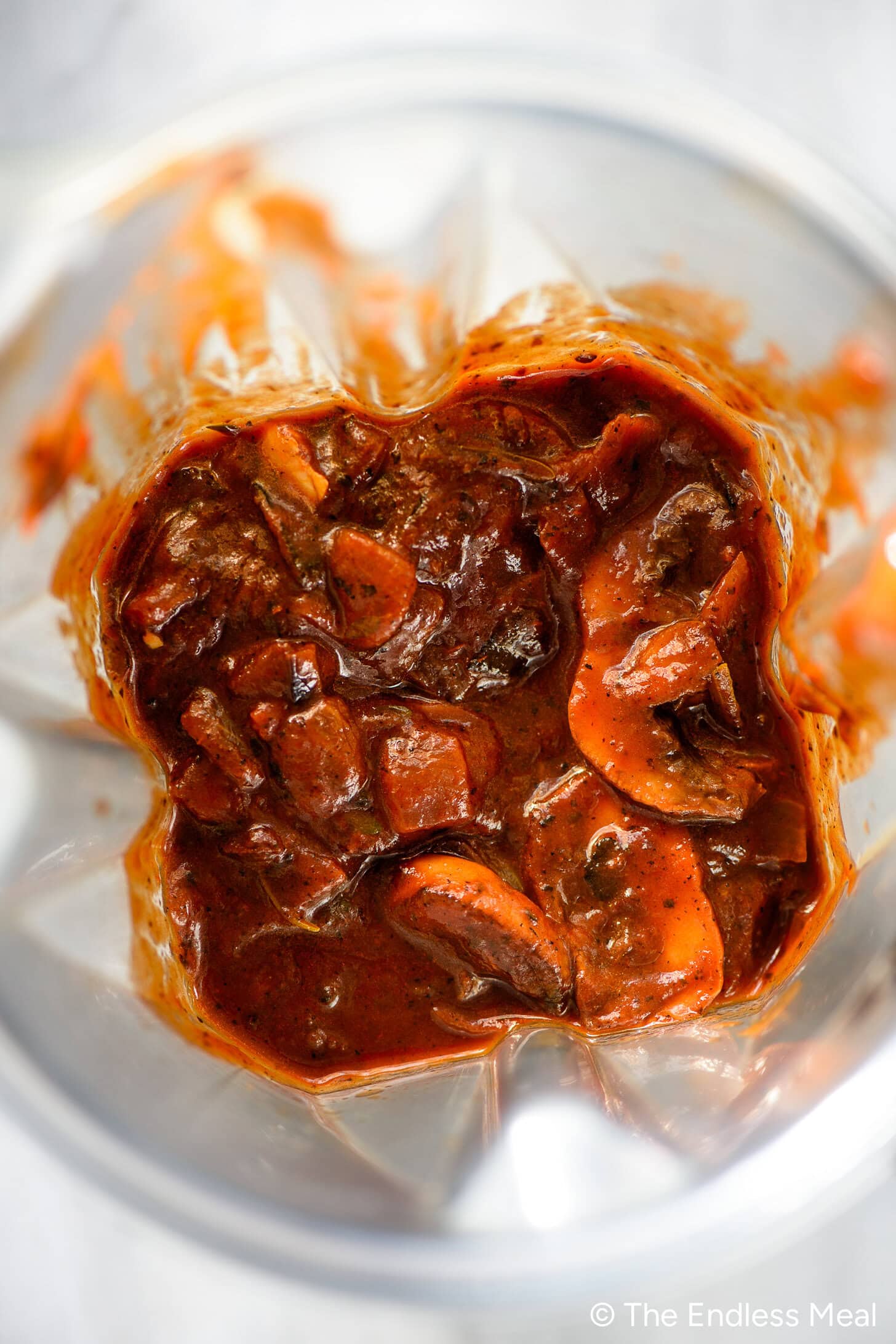 Top-down view of a blender containing chunky red sauce with sliced mushrooms and vegetables, perfect for making a savory mushroom gravy.