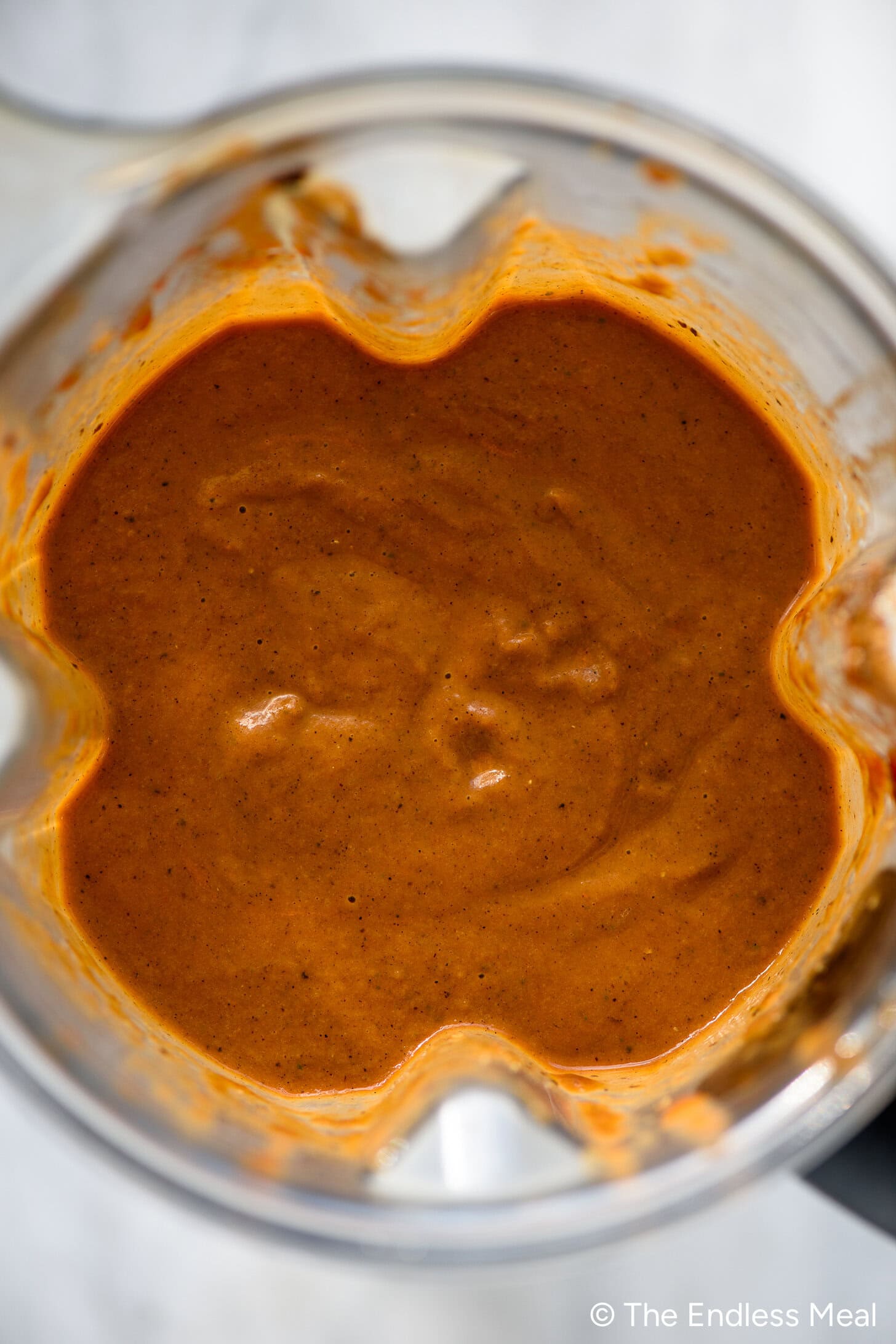 Blender filled with smooth, reddish-brown mushroom gravy or dressing, viewed from above on a light surface.