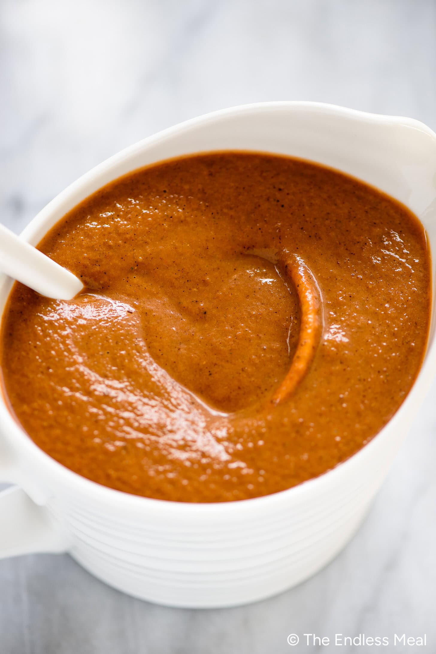 A white bowl filled with thick, reddish-brown mushroom gravy, with a white spoon resting inside.