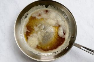A stainless steel pan with browned butter and foam, perfect for starting a delicious Honey Garlic Carrots dish, rests on a white marble surface.