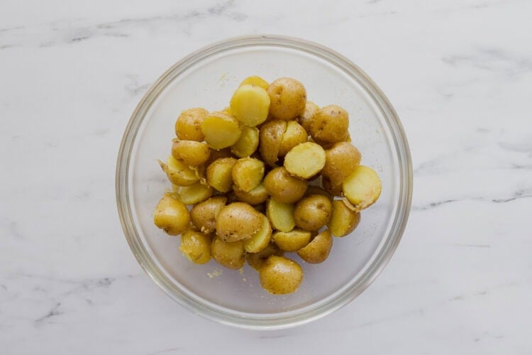 A clear glass bowl filled with halved baby potatoes on a white marble surface.