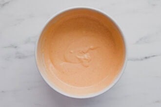 A white bowl filled with smooth, light orange sauce sits on a white marble surface.