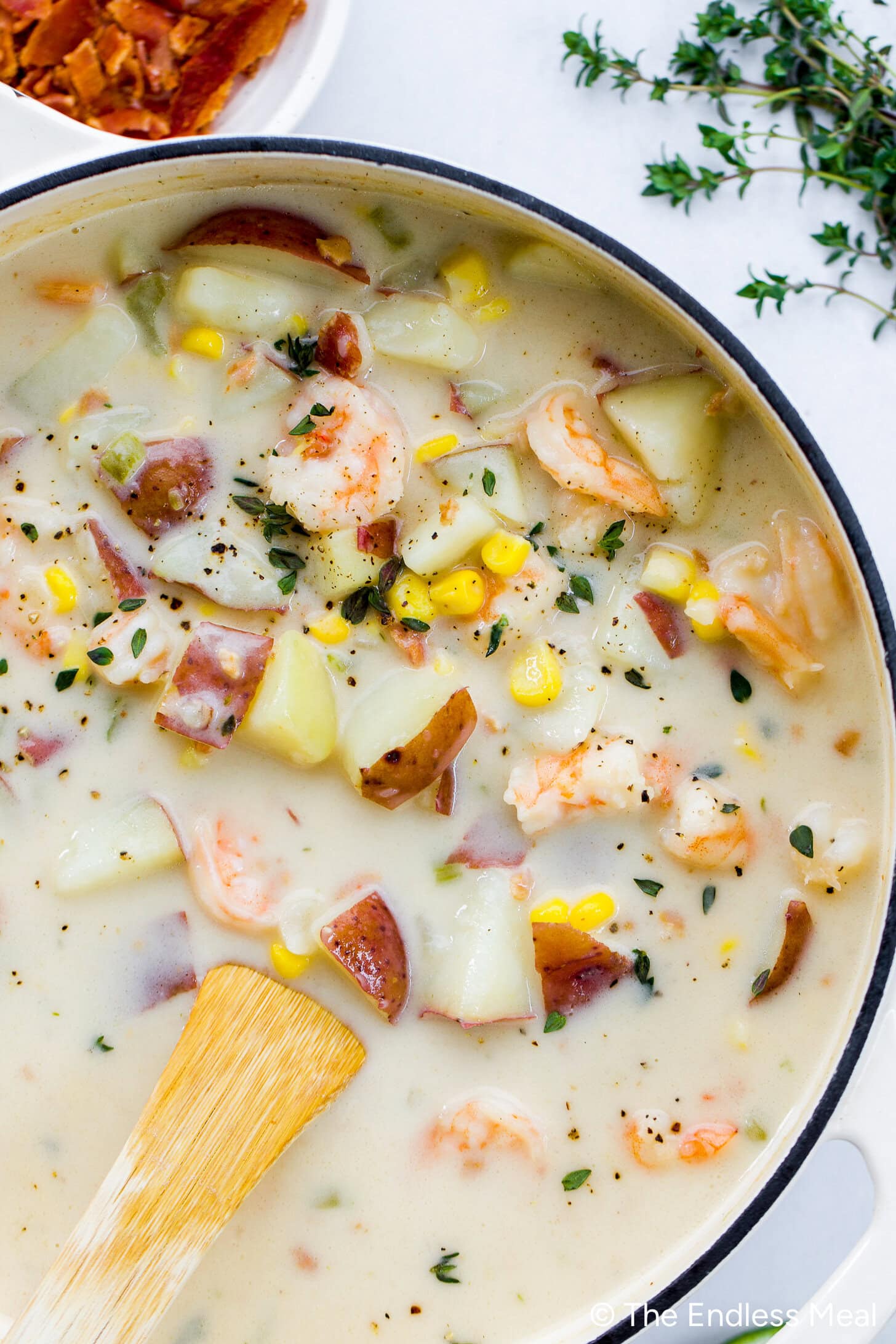 A pot of creamy chowder with shrimp, potatoes, corn, and herbs is being stirred with a wooden spoon, filling the kitchen with the comforting aroma of homemade shrimp chowder.