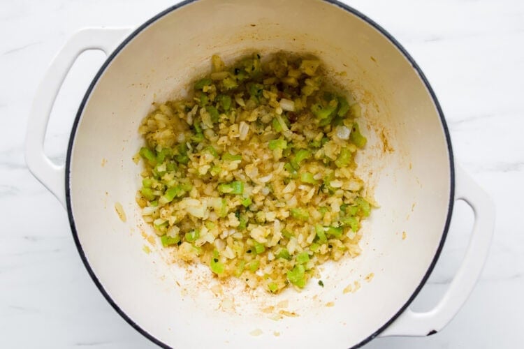 Chopped onions and celery sautéing in a white pot on a marble surface, perfect as the flavorful base for a creamy chowder.