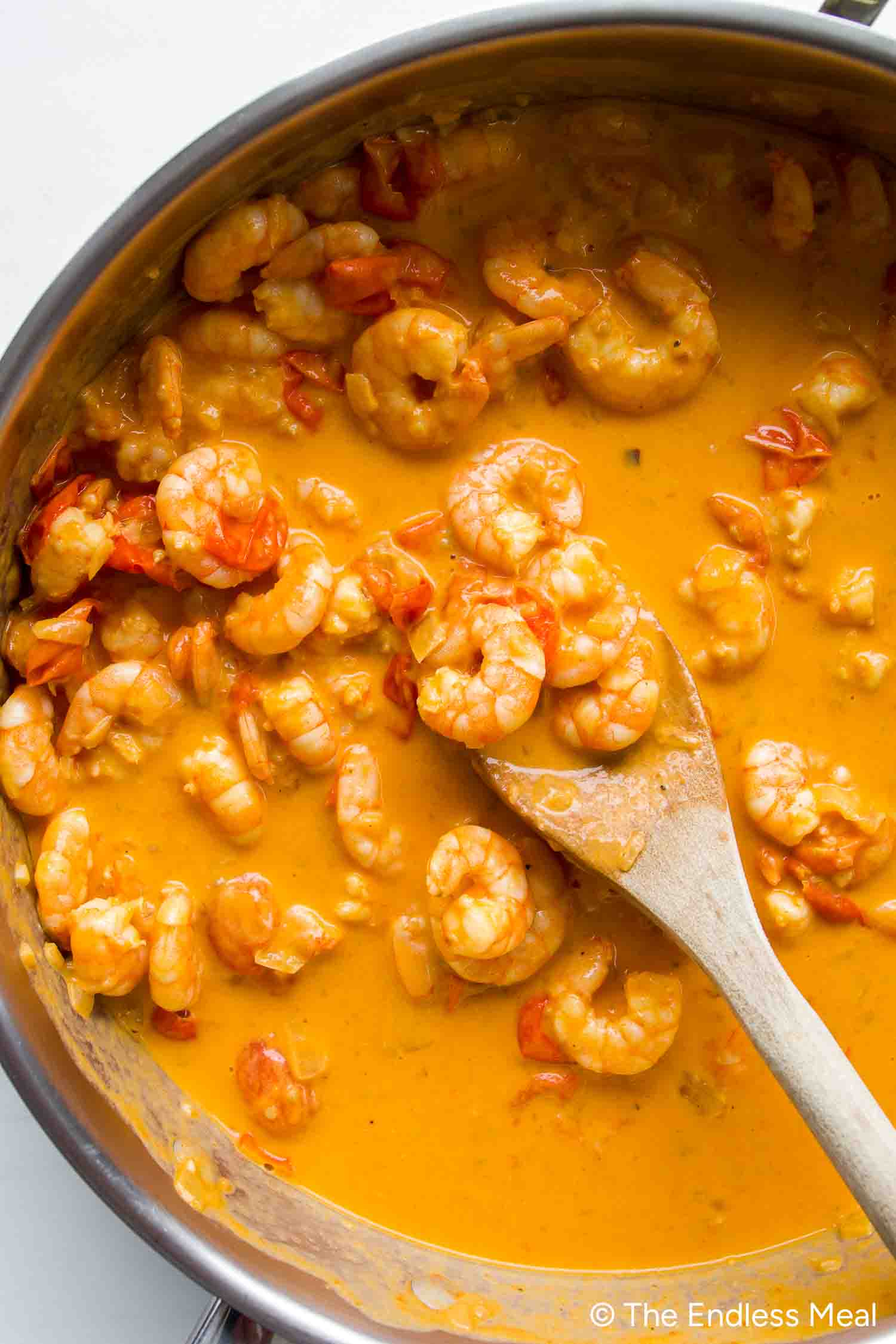 Shrimp cooked in a creamy orange sauce with chopped tomatoes, stirred with a wooden spoon—perfect for making Creamy Tomato Shrimp Pasta.