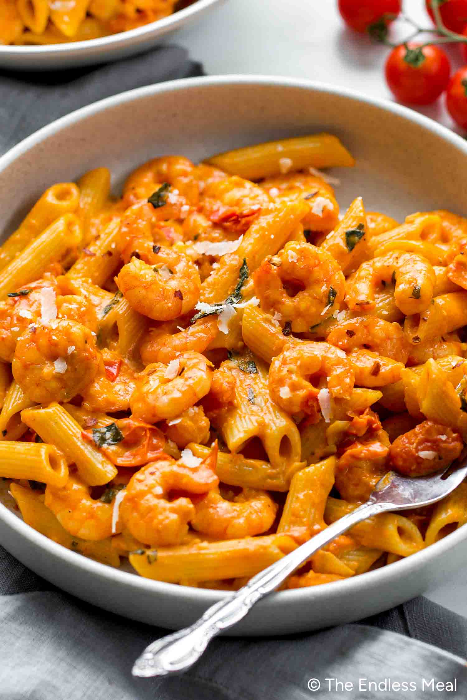 A bowl of creamy Tomato Shrimp Pasta with penne, garnished with fresh herbs and grated cheese, sits alongside a ready-to-use fork.