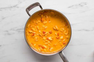 A stainless steel pan filled with Creamy Tomato Shrimp Pasta and pieces of seafood sits on a white marble countertop.