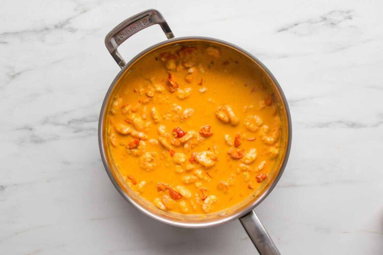 A stainless steel pan filled with Creamy Tomato Shrimp Pasta and pieces of seafood sits on a white marble countertop.