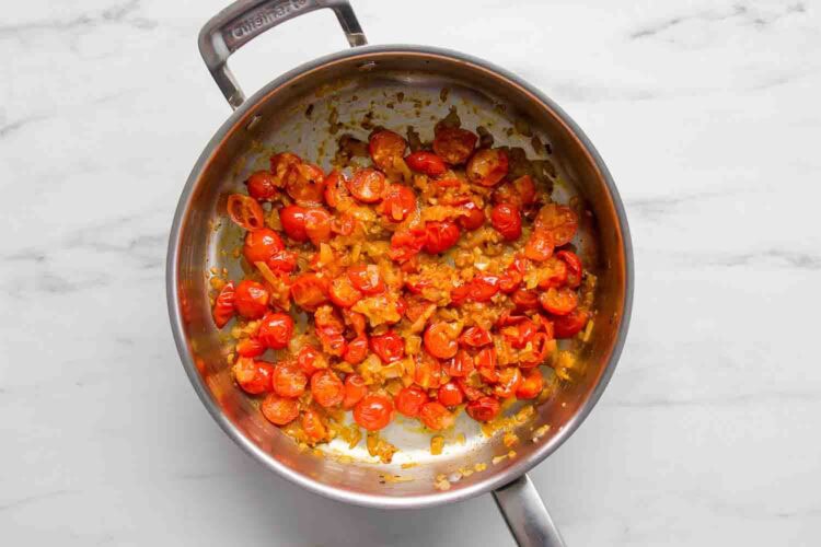 Sautéed cherry tomatoes and onions cooking in a stainless steel pan on a marble countertop, perfect for preparing creamy tomato shrimp pasta.